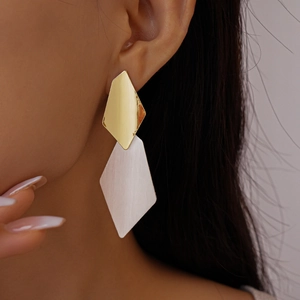 Detail view of rhombic brushed metal drop earrings worn by a model in a golden finish