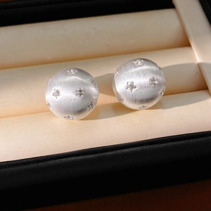 Gros plan détaillé de boucles d'oreilles boules brossées argentées avec cristaux étoiles.