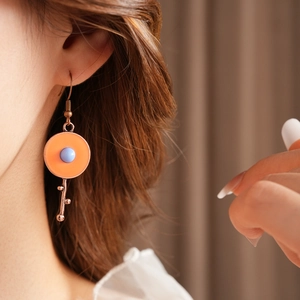 Detail of vintage enamel earrings with orange base and blue bead on model ear