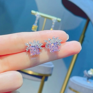 Pink radiant cut diamond stud earrings in silver settings shown on fingertips
