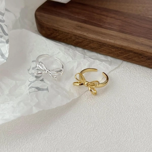 Detail of adjustable silver and gold bow rings on a minimalist aesthetic background