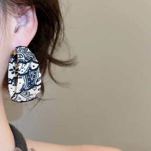 Détail d'une créole en forme de C avec revêtement en tissu noir et blanc et tige dorée