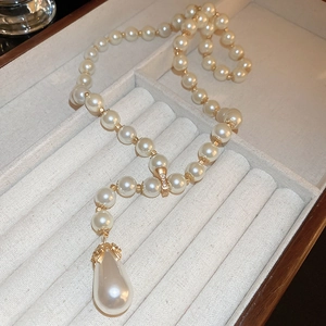 Close-up of a Y-shaped gold necklace with white teardrop pearls in a beige velvet jewelry box
