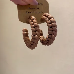 Handcrafted brown leather woven C-shape hoop earrings with silver needle on display