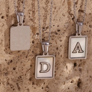 Macro detail of silver titanium steel D and A letter pendants with white shell inlay