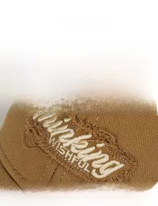 Detailed view of white WISHFUL embroidery with distressed frayed edges on a brown cotton cap