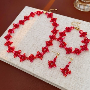 Three-piece red beaded jewelry set with floral necklace, bracelet, and drop earrings