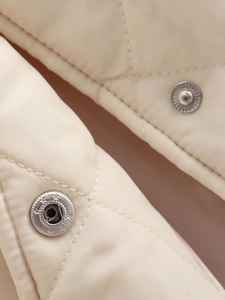 Gros plan d'une veste matelassée beige montrant la texture et les boutons pression étoilés