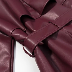 Détail du manteau en cuir bordeaux montrant le grain texturé et les coutures avec ceinture