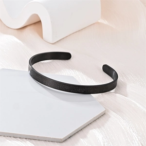 Primer plano de brazalete abierto en C de acero de titanio esmerilado negro moda