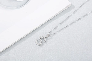 Macro shot of silver letter S pendant with rhinestones and SMILE engraving on fine chain