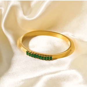 Detail of gold-plated stainless steel bracelet with green rectangular zircons on silk