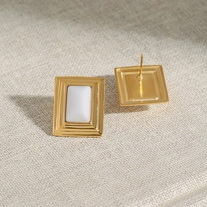 Detail of gold geometric earrings with white rectangular inlay on textured fabric