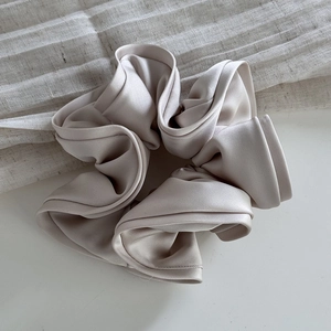 Elegant champagne satin scrunchie with ruched texture on a neutral linen background