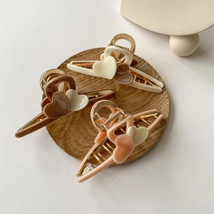 Three elegant heart-shaped claw clips in cream, brown, and pink tones on a wood base