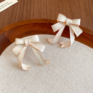 Close-up of cream bow earrings with rose gold edges on a rustic linen background