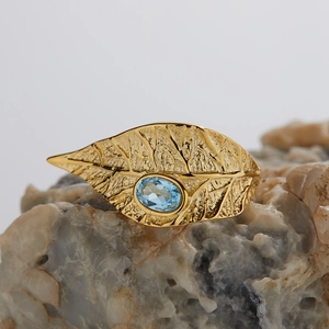 Detailed macro shot of a gold leaf-shaped ring with a sky blue gemstone on stone