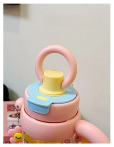 Detail van de roze en gele beker met ringhandvat, klapdeksel en smiley bloemhanger