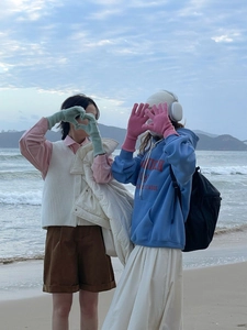 Primer plano de amigas con guantes de lana coloridos formando un corazón en la playa