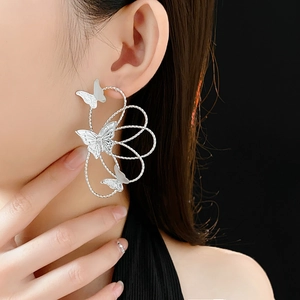 Detail of silver hollow butterfly drop earrings worn by a model on black background