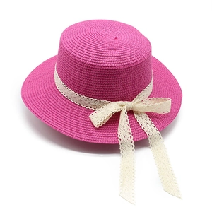 Detail of fuchsia straw hat with intricate white lace ribbon and decorative bow