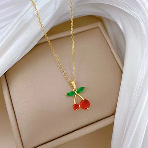 Detailed macro of a gold cherry pendant necklace resting on elegant white silk fabric