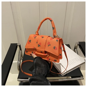 Detail van oranje handtas met aardbeienprint en lycheepatroon op een designstoel