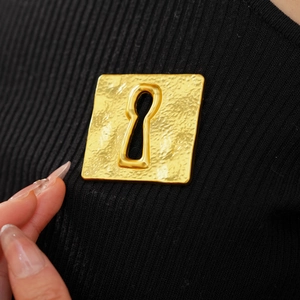 Close-up of vintage golden square brooch with keyhole design on black knitwear