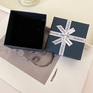 Detail showing an open dark blue jewelry box with a white satin ribbon and black velvet lining