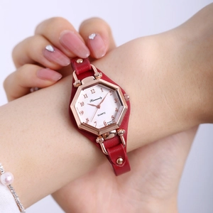 Détail d'une montre à quartz dorée avec bracelet en cuir rouge portée par une femme