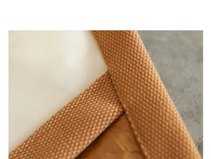 Detailed macro view of off-white canvas fabric with brown woven trim and stitching