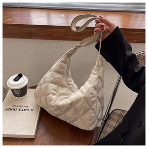 Close-up of beige quilted nylon crossbody bag on a wooden table in a cozy cafe