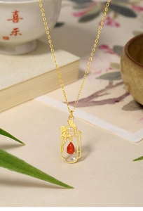 Detailed close-up of 925 silver ginkgo pendant with red agate teardrop on golden chain