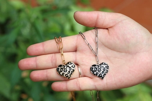 Detail of 18K gold and silver heart pendants with leopard print and paperclip chain