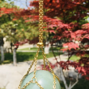 Close-up of golden mesh net pendant holding a smooth light green gemstone outdoors