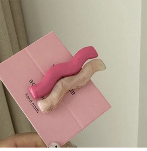 Detail view of wavy resin hair clips in rose pink and beige marble on a display card
