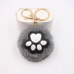 Close-up of grey plush cat paw pompom keychain with white pads and gold metal ring
