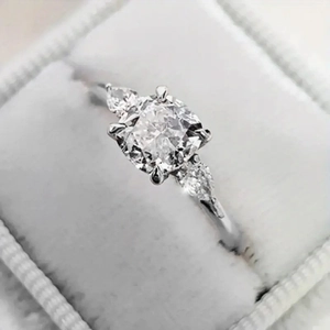 Driesteens ring met kussengeslepen zirkonia en zijstenen in een fluwelen doosje