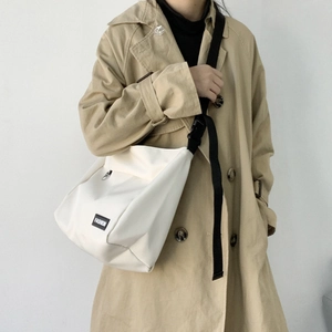 Detailed view of white canvas crossbody bag with adjustable black strap on a khaki trench coat