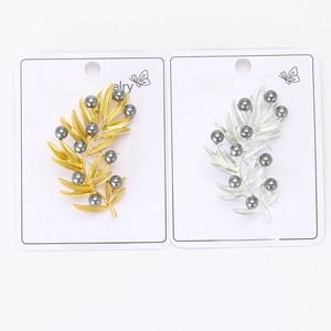 Detailed shot of leaf-shaped pearl brooches in matte gold and silver on display cards