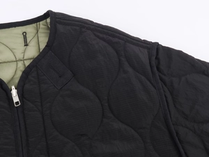 Detail of wavy quilted stitching on reversible black and olive green jacket with silver zipper
