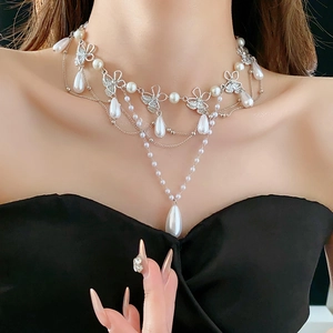Close-up of layered butterfly necklace with teardrop pearls and rhinestones on a model