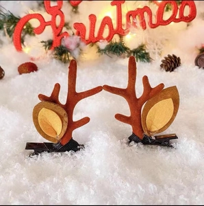 Close-up of brown plush reindeer antler hair clips on white snow with festive Christmas decor
