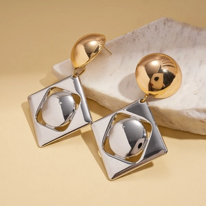 Detailed close-up of geometric gold and silver metallic square earrings on a stone base