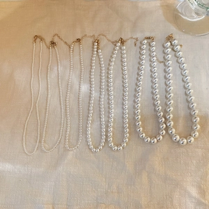 Comparison of seven pearl necklaces in varying sizes with gold clasps on beige fabric