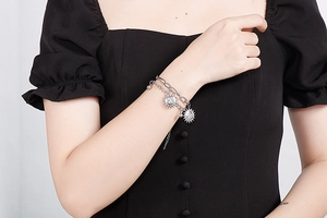 Detail view of a double-layered silver sun pendant bracelet on a person's wrist