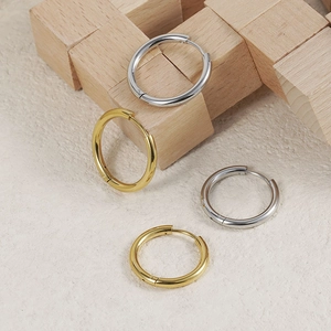 Polished gold and silver stainless steel hoop earrings on minimalist wooden display