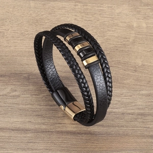 Detail of multi-layer black braided leather bracelet with gold metal rings on wood surface