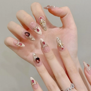 Detalle de uñas postizas almendradas rojas con pedrería de lujo y perlas