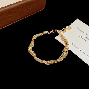 Detail view of a multi-layer gold braided metal bracelet with gold beads on black background